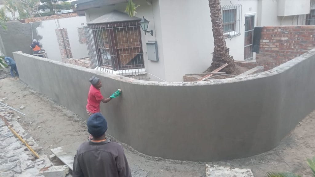 Builder plastering a curved boundary wall at a Cape Town home