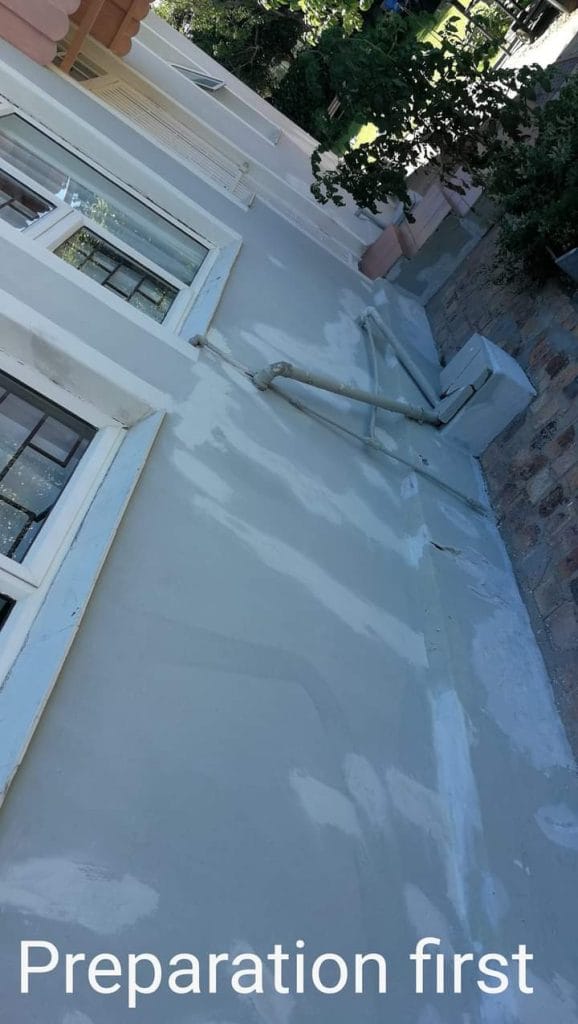 Grey liquid waterproofing coat applied to a flat roof section beside a Cape Town home