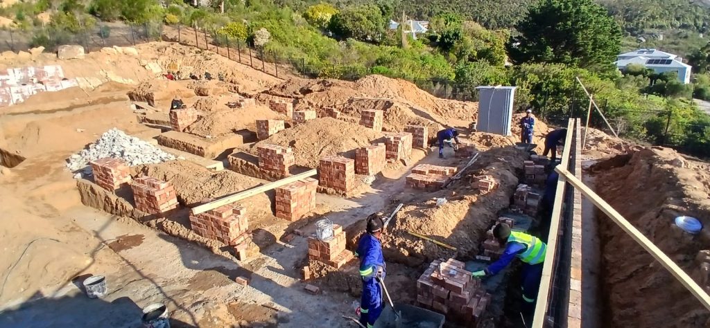 Builders working on brick foundation walls on a hillside site